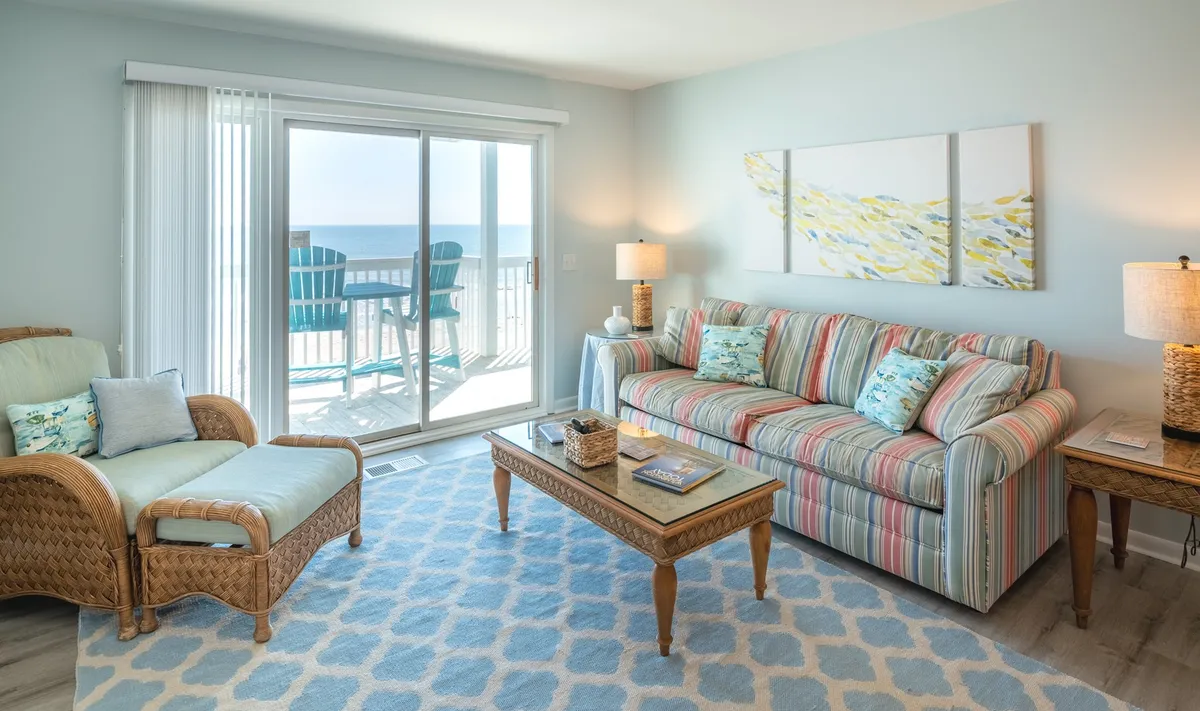A cheerful and serene living room with a plush sofa, coffee table, tasteful decorative artwork, and a sliding glass door opening to expansive ocean views. The space is bathed in natural light, inviting both relaxation and social gatherings while providing a direct visual connection to the ocean.