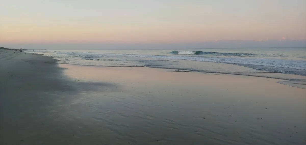Expansive view of the beach with gentle ocean waves and a soft sky, inviting guests to enjoy the classic beach experience—walking, playing, or simply soaking in the serene atmosphere.