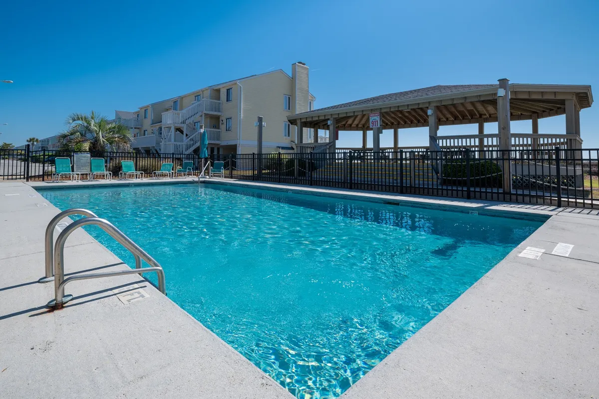 This exterior image features a sparkling swimming pool surrounded by lounge chairs and a shaded gazebo, set within a relaxed resort environment. The area invites families to swim, sunbathe, and socialize while enjoying leisure time together at the property.