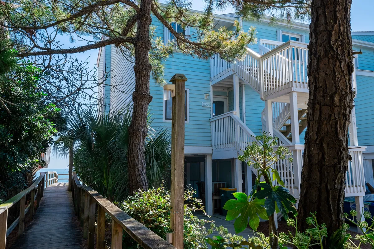A blue-sided building surrounded by lush greenery, with a wooden pathway inviting visitors to wander through the landscaped grounds. The scene feels peaceful, hinting at easy outdoor access for nature strolls and relaxation.