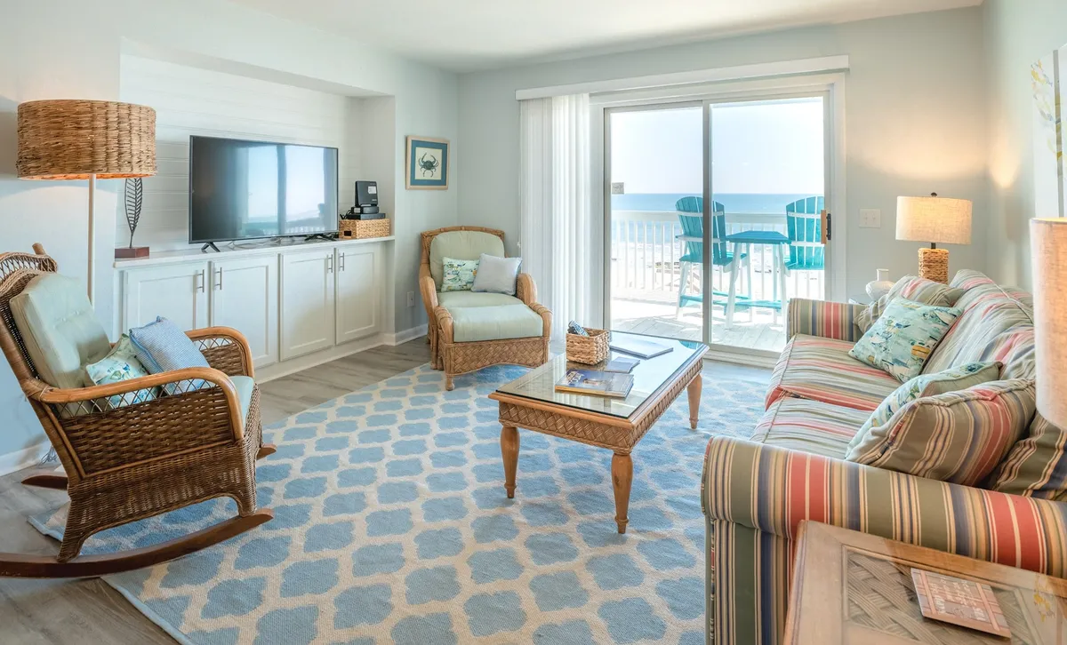 This inviting living room features a comfortable sofa adorned with colorful cushions, a classic rocking chair, and a coffee table, all set before large glass doors that open to a private balcony with sweeping sunrise ocean views.