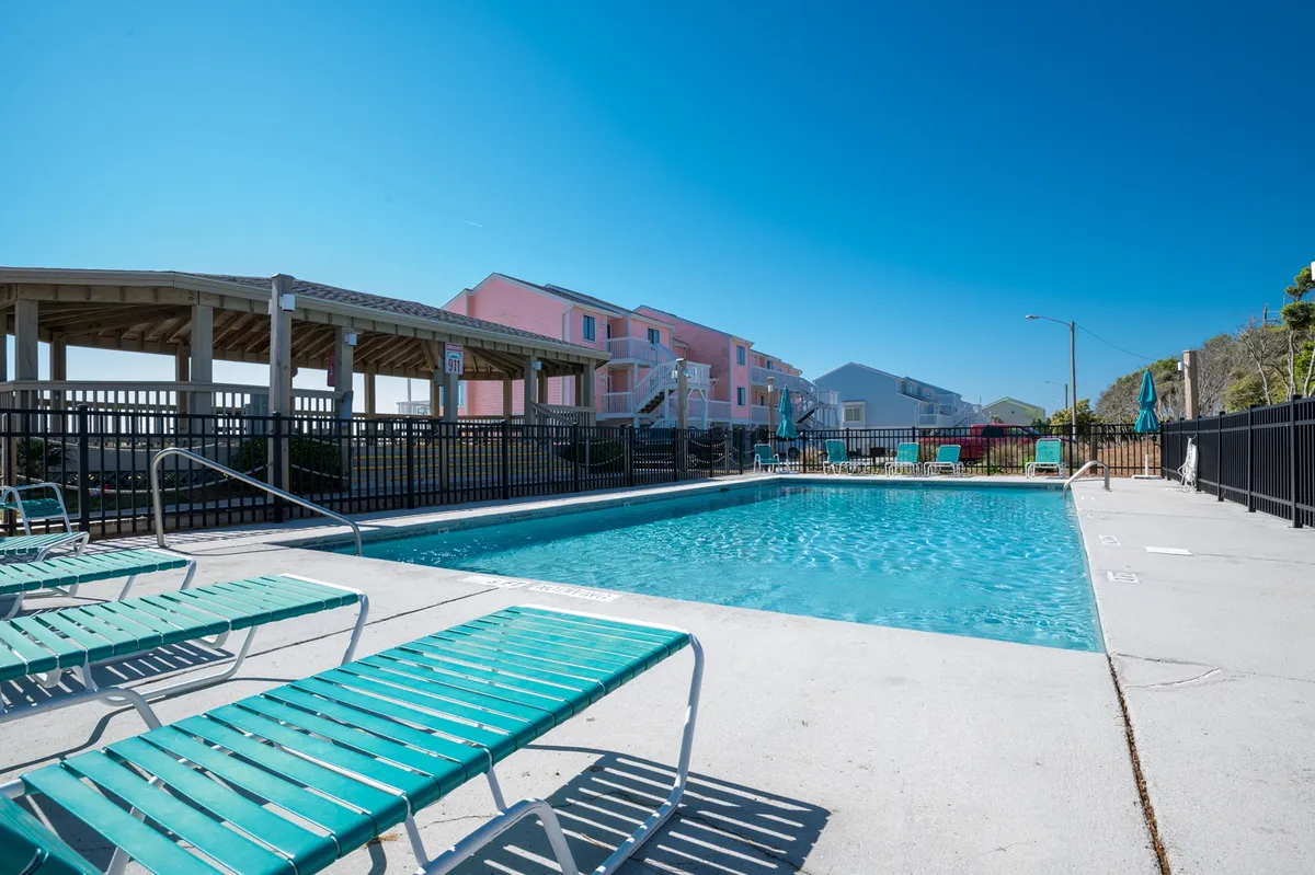 A sparkling swimming pool lined with lounge chairs, with colorful buildings creating a cheerful backdrop. The area is open and accessible, inviting guests to swim, sunbathe, or relax by the water.