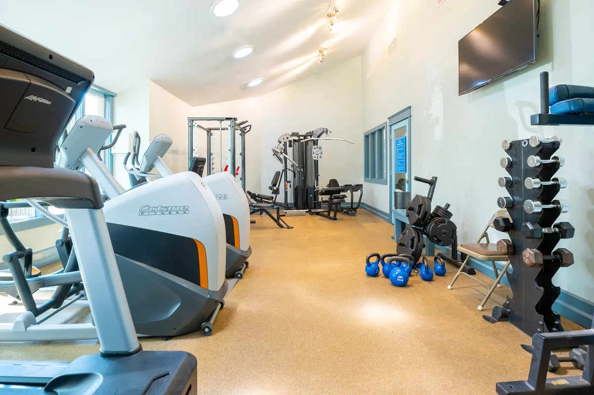A modern fitness center is depicted, featuring treadmills, weightlifting equipment, kettlebells, and other exercise machines. The space is bright and energizing, designed for both personal and group workouts.